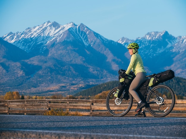 Kobieta podróżuje po terenie mieszanym wycieczki rowerowe z bikepackingiem Podróżnik podróż z torbami rowerowymi Turystyka sportowa bikepacking rower odzież sportowa w kolorach zielono-czarna Góra śnieg nakryty