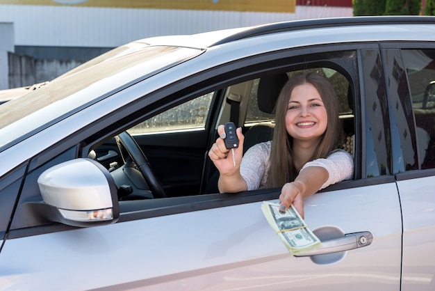 Kobieta pokazująca dolary i klucze z okna samochodu