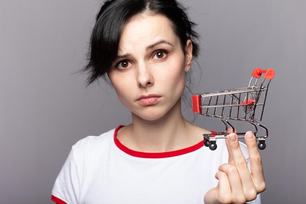 Kobieta pokazująca mini koszyk na zakupy sklep internetowy koncepcja e-commerce Szare tło