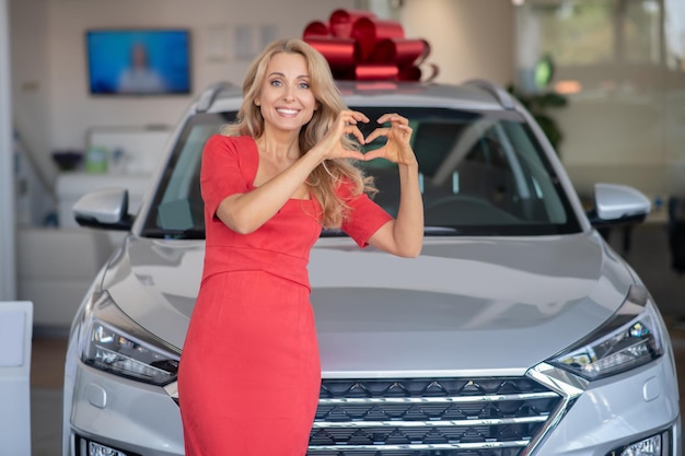 Kobieta pokazująca znak serca stojący w pobliżu nowego samochodu