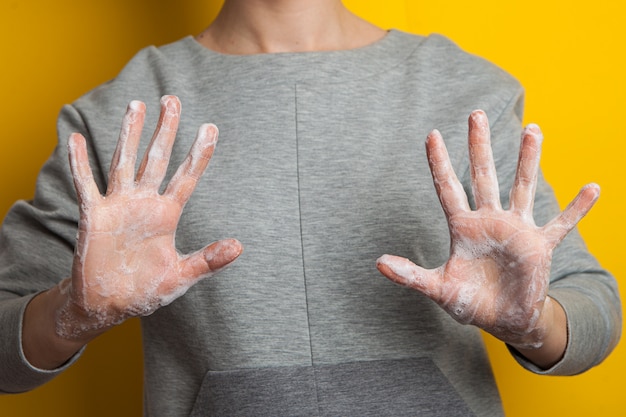 Kobieta pokazuje mydlane ręce. żółta jasna ściana, odizolowywająca. dezynfekcja rąk, aby zapobiec koronawirusowi.