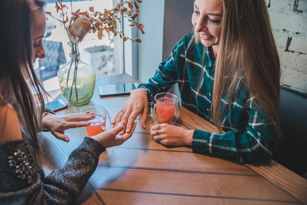 Kobieta pokazuje pierścionek zaręczynowy przyjacielowi w kawiarni, pijąc rozgrzaną herbatę owocową