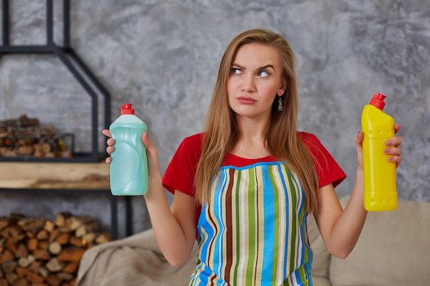 Kobieta Porównuje Dwie Butelki Detergentu W Domu Do Czyszczenia W Salonie. Praca Domowa. Miejsce Na Tekst Na Butelce