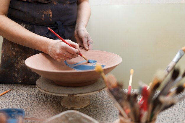 Kobieta Potter maluje talerz ceramiczny.