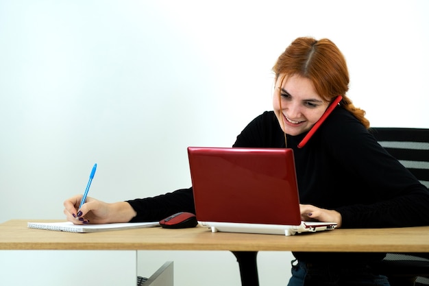 Kobieta Pracownik Biurowy Młodych Rozmawia Przez Telefon Komórkowy Siedzi Za Biurkiem Z Komputera Przenośnego I Notebooka.