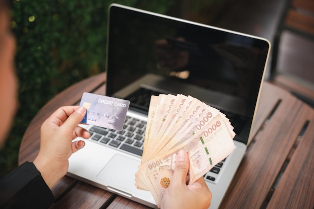 Zdjęcie kobieta pracująca i robiąca zakupy na świeżym powietrzu w kawiarni kawiarni internetowa bankowość internetowa e-commerce ręce biznesmenki trzymającej tajskie pieniądze i kartę kredytową na laptopie technologia finanse