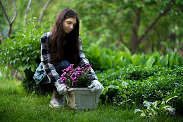 Kobieta pracująca na zewnątrz w ogrodzie i trzymająca doniczkę z posadzonymi w niej kwiatami