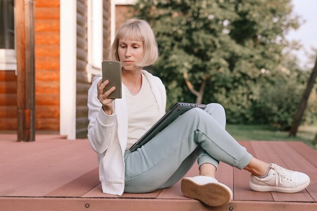 Kobieta pracująca w parku z telefonem i laptopem Kobieta pracuje na świeżym powietrzu zielonym tle przyrody Połączenie sieci Wi fi bezpłatny dostęp Freelancer Relaks w naturze i korzystanie z technologii