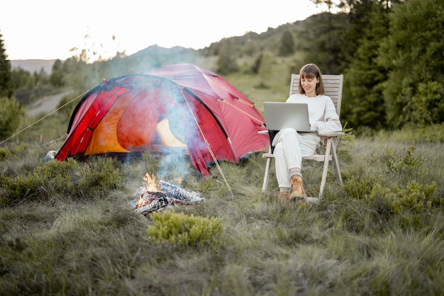Kobieta pracuje na laptopie, siedząc zrelaksowana przy ognisku w górach