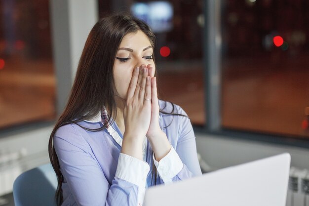 Kobieta pracuje przy stole z laptopem w nocy w biurze. Za oknem świecą wielokolorowe światła
