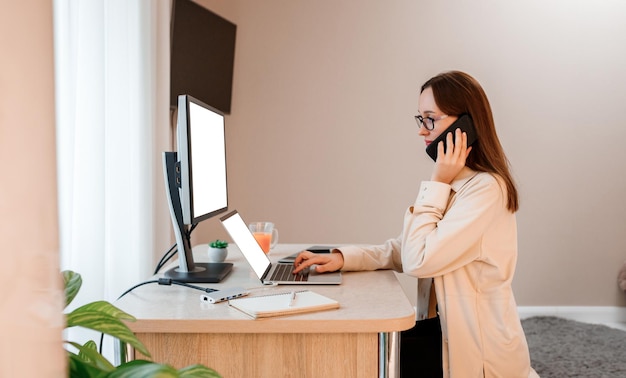 Kobieta pracuje w domowym biurze na laptopie i rozmawia przez telefon z klientami Młoda szczęśliwa studentka studiuje na uniwersytecie online