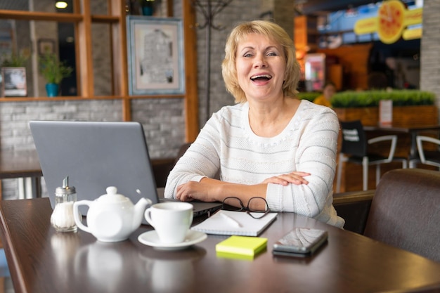 Kobieta pracuje z laptopem przy stoliku w kawiarni lub w biurze. Kobieta w średnim wieku pracuje zdalnie. Ona jest bizneswoman.