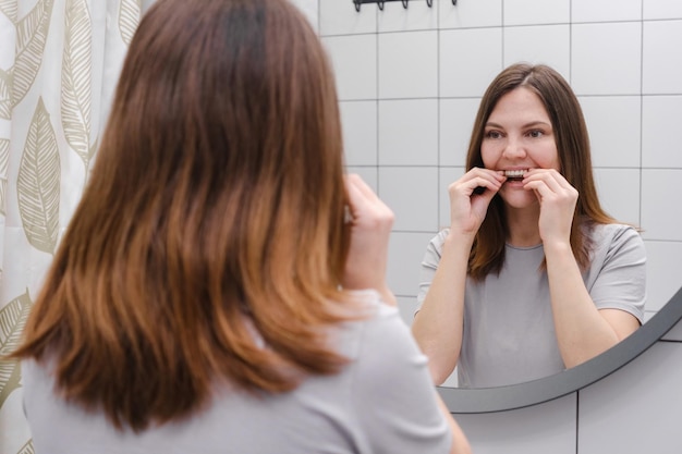 Kobieta przed lustrem w łazience zakłada niewidoczne plastikowe nakładki na zęby lub aparat ortodontyczny Piękny i zdrowy uśmiech Wybielanie zębów