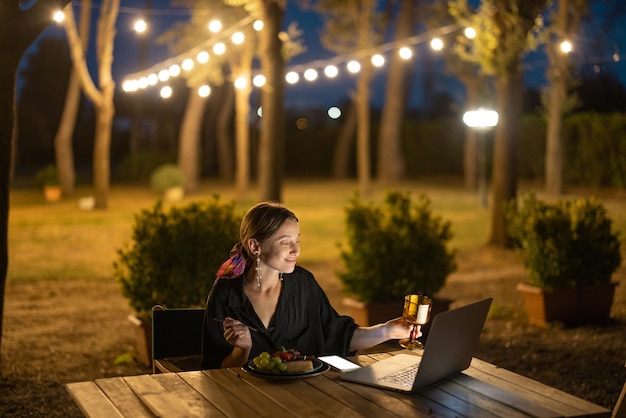 Kobieta przeprowadzająca wideorozmowę i wznosząca toast za laptopa