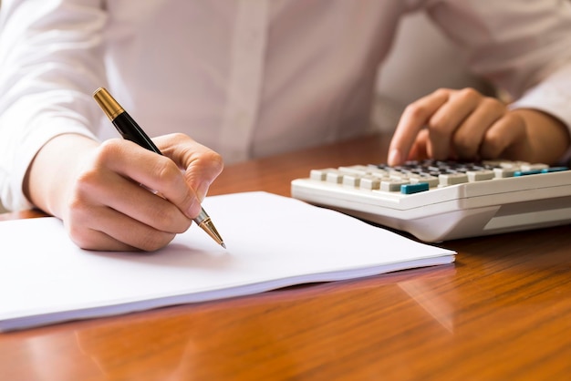 Kobieta przy biurku, korzystająca z kalkulatora i pisząca na białym papierze