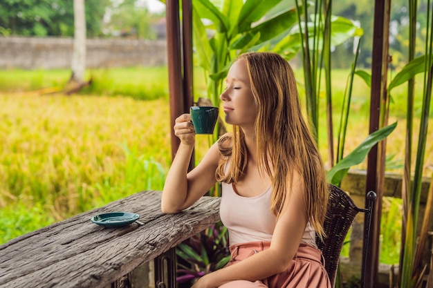 Kobieta przy filiżance kawy na werandzie kawiarni w pobliżu tarasów ryżowych na Bali, Indonezja.