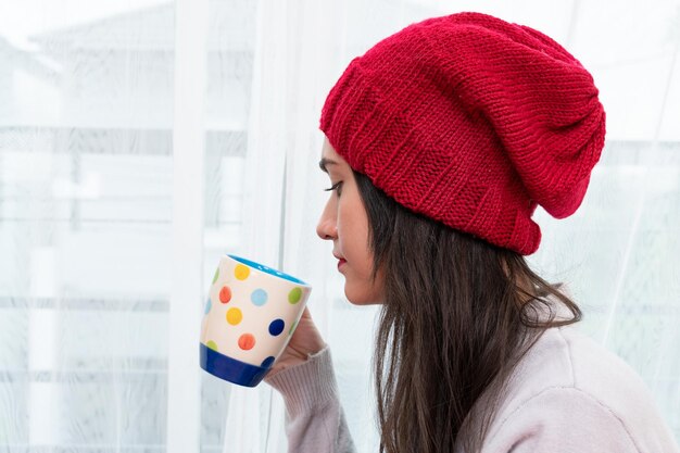 Zdjęcie kobieta przy oknie trzymająca filiżankę kawy