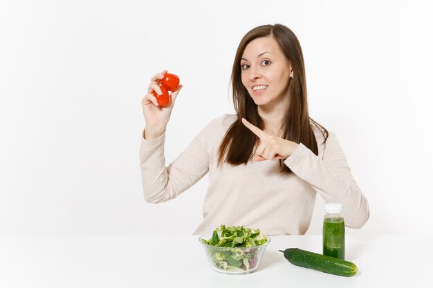 Kobieta przy stole z zielonymi koktajlami detox, świeże sałatki w szklanej misce, pomidor, ogórek na białym tle. Prawidłowe odżywianie, jedzenie wegetariańskie, zdrowy styl życia, koncepcja diety. Skopiuj miejsce.