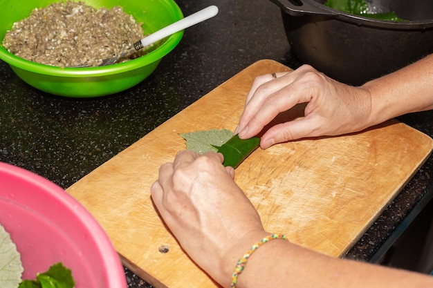 Kobieta przygotowuje jedzenie w domu Mięso mielone zawija się w liście winogron na drewnianej desce dolma