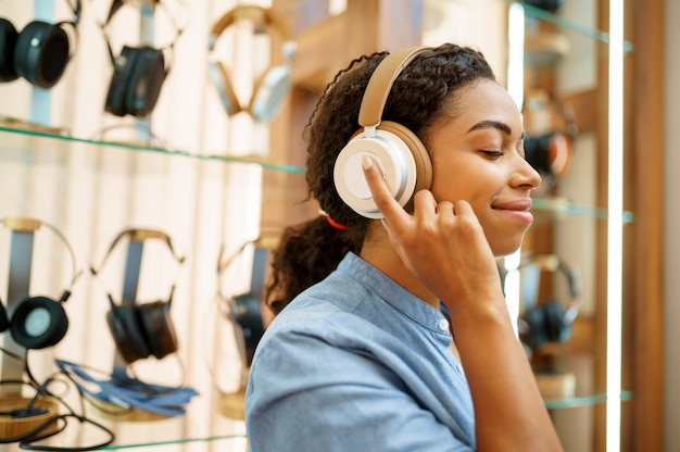 Kobieta przymierzająca słuchawki w sklepie akustycznym, widok z tyłu. Kobieta w sklepie audio, gablota ze słuchawkami, kupujący w sklepie multimedialnym