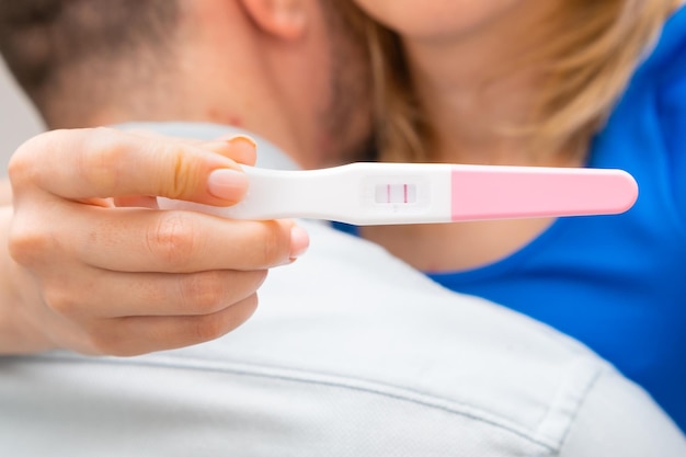Zdjęcie kobieta przytulająca mężczyznę i trzymająca pozytywny test ciążowy
