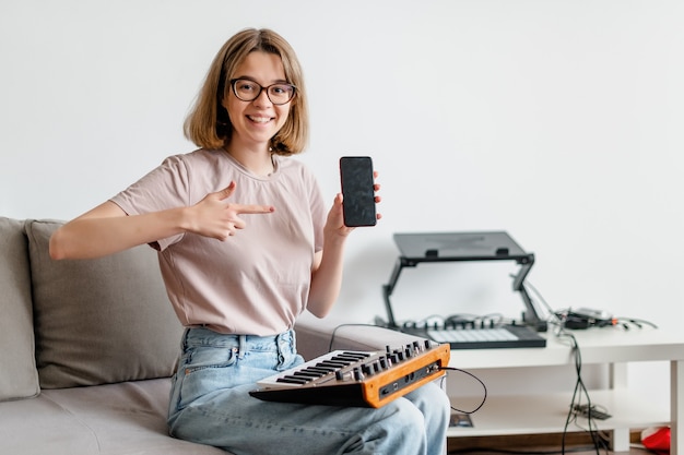 Kobieta ręce grając na syntezatorze minilogue za pomocą aplikacji mobilnej, pokazując kciuk do góry w domu