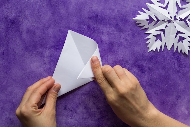 Kobieta ręce składa trójkątny arkusz papieru na pół, aby zrobić mniejszy trójkąt na fioletowej powierzchni