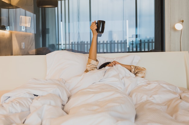 Kobieta ręce trzymając filiżankę kawy nad kocem w łóżku.