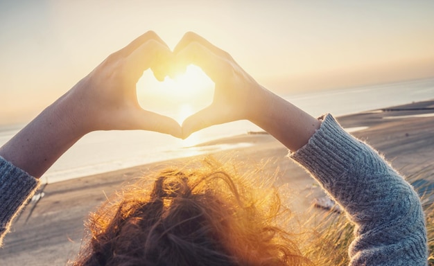 Kobieta ręce w symbol serca w kształcie światła słońca na plaży obraz koncepcyjny stylu życia i uczuć