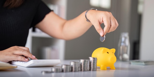 Kobieta ręcznie wkłada monety do świnki, by zaoszczędzić pieniądze i oszczędzić pieniądze.