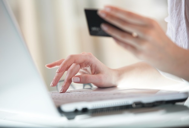 Kobieta ręcznie wprowadza dane za pomocą laptopa, trzymając w drugiej ręce kartę kredytową