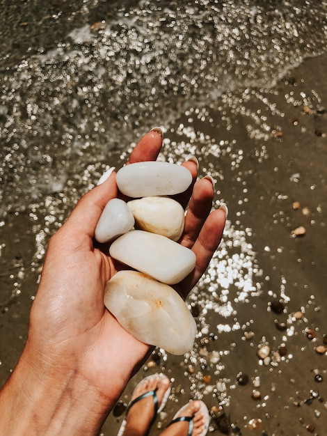 Kobieta Ręka Do Manicure Trzymając Białe Piękne Kamienie Nad Morzem Piaszczystej Plaży Latem. Naturalne Tło