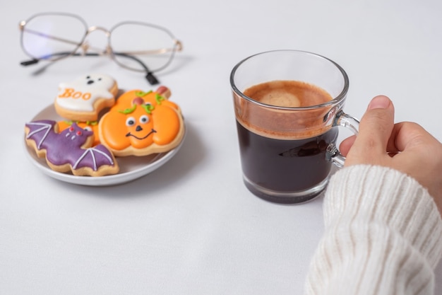 Kobieta ręka trzyma filiżankę kawy podczas jedzenia śmieszne Halloween Cookies. Happy Halloween Day, Trick or Threat, Hello October, jesień jesień, tradycyjna, imprezowa i świąteczna koncepcja