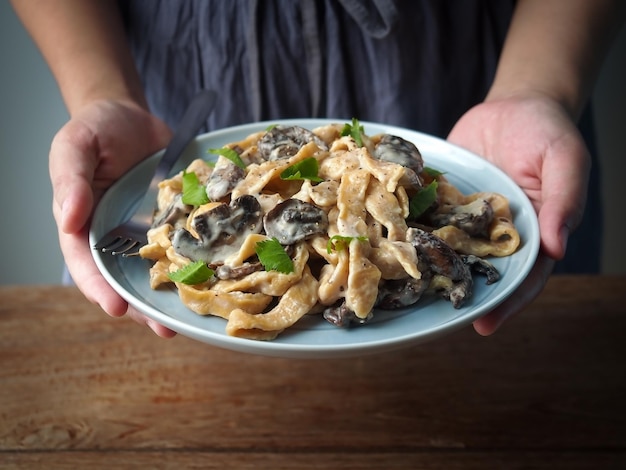 Kobieta ręka trzyma naczynie z domowym makaronem z pieczarkami i sosem carbonara.