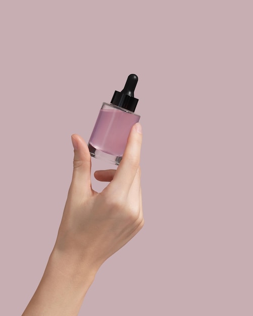 Kobieta ręka trzyma opakowanie olejku do twarzy lub serum na różowym tle Kosmetyczny produkt kosmetyczny do koncepcji pielęgnacji skóry makieta