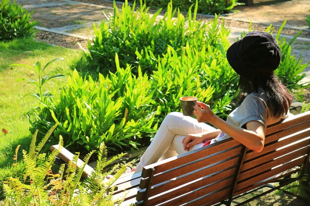 Kobieta Relaksuje Na Drewnianej ławce W żywym Zielonym Ogródzie Trzyma Filiżankę Gorąca Kawa