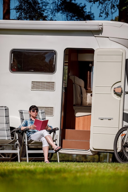 Kobieta relaksuje się i czyta książkę w pobliżu kempingu. Wakacje w przyczepie kempingowej. Rodzinna podróż na wakacje, wyjazd na wakacje w kamperze RV.