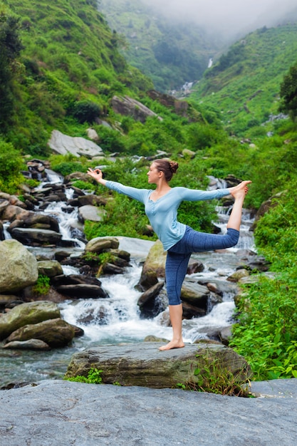 Kobieta robi joga asana Natarajasana na zewnątrz przy wodospadzie