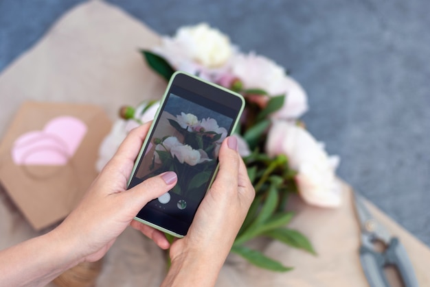 Kobieta robi mobilne zdjęcie świeżych kwiatów, kwiaciarnia robi bukiet i robi zdjęcie telefonem dla sieci społecznościowych