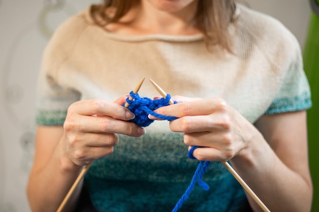 Kobieta robi na drutach sweter z niebieskiej przędzy