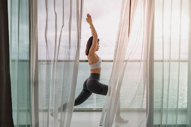 Kobieta robi pozę wojownika jogi na balkonie z widokiem na morze