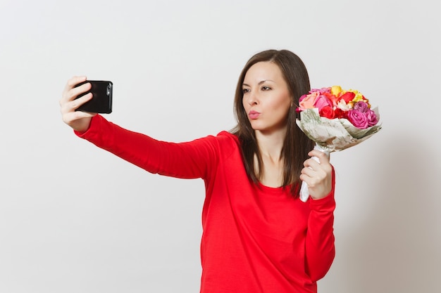 Kobieta robi selfie kaczka twarz na telefon komórkowy z bukietem pięknych kwiatów na białym tle. Skopiuj miejsce na reklamę. Walentynki, Międzynarodowy Dzień Kobiet, koncepcja świąteczna