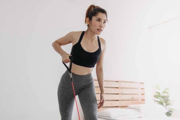Kobieta robi taśmę oporową ćwicząc kosiarkę w swojej sypialni