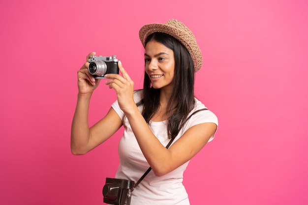 Kobieta robi zdjęcia trzymając aparat fotograficzny, odizolowane na różowo.