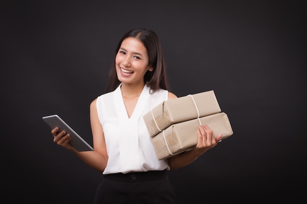 Kobieta robiąca zakupy online za pomocą tabletu, trzymająca pudełko do dostawy paczek