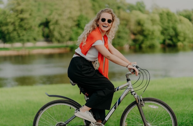 Kobieta rowerzysta jeździ rowerem, uśmiecha się do kamery, nosi codzienne ubrania