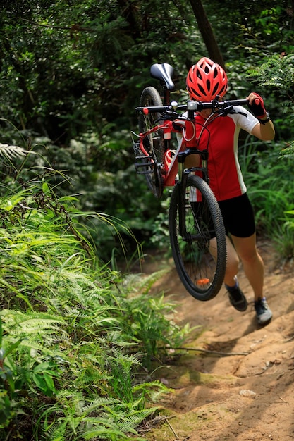 Kobieta-rowerzysta niesie rower górski spacerując szlakiem lasu tropikalnego