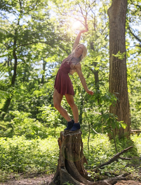 Zdjęcie kobieta równoważąca się na pniu drzewa z ręką podniesioną w lesie
