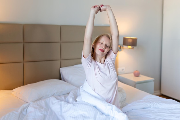 Kobieta rozciągająca się w łóżku z podniesionymi rękami Portret atrakcyjnej uroczej dziewczyny cieszącej się czasem w złych po spaniu leżącym pod kocem, co rozciąganie z zamkniętymi oczami Dobry dzień życia zdrowie