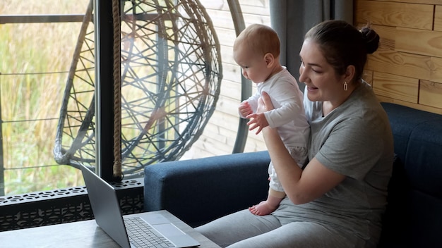 Kobieta rozmawia przez połączenie wideo przez laptopa, trzymając dziecko na kolanach